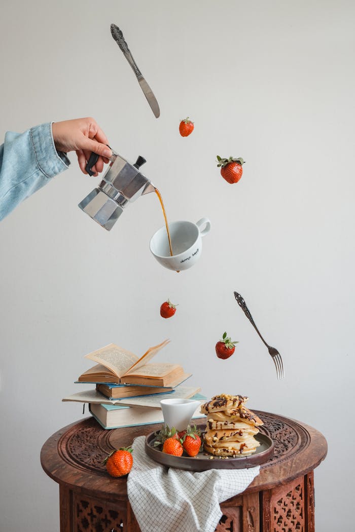 Creative composition of floating coffee, pancakes, strawberries, and cutlery for a unique culinary art scene.
