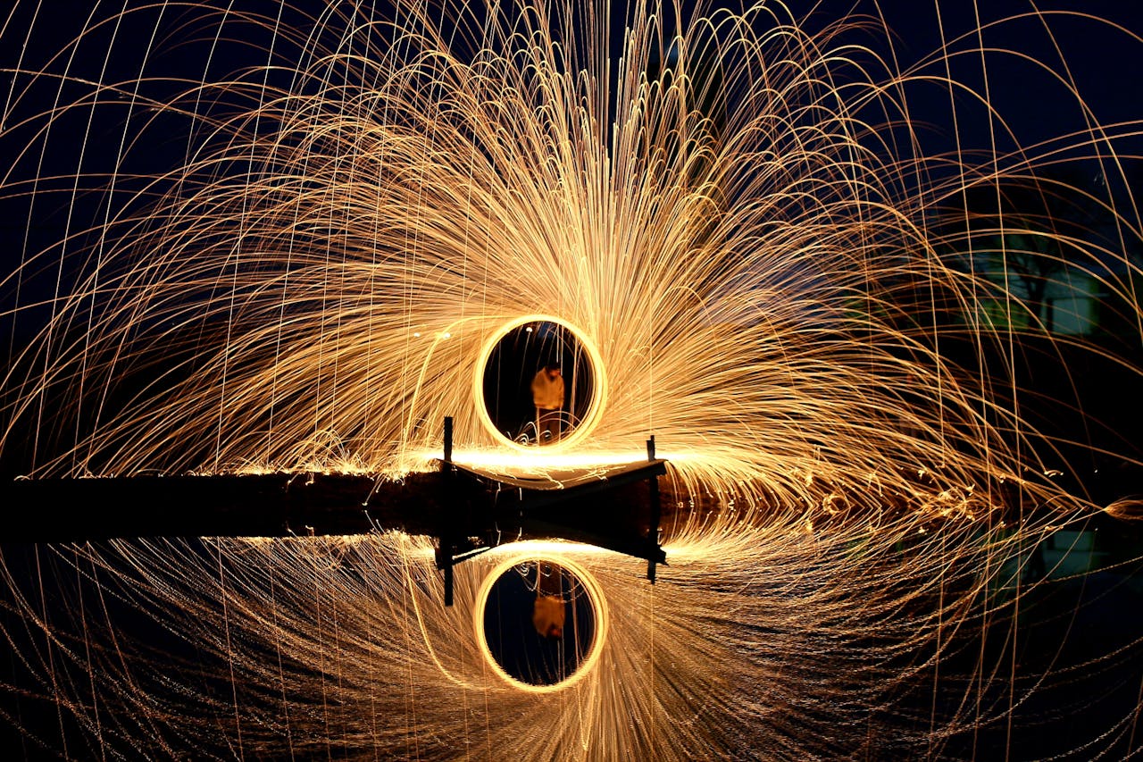 Steel wool light painting creating stunning circle of sparks over water.